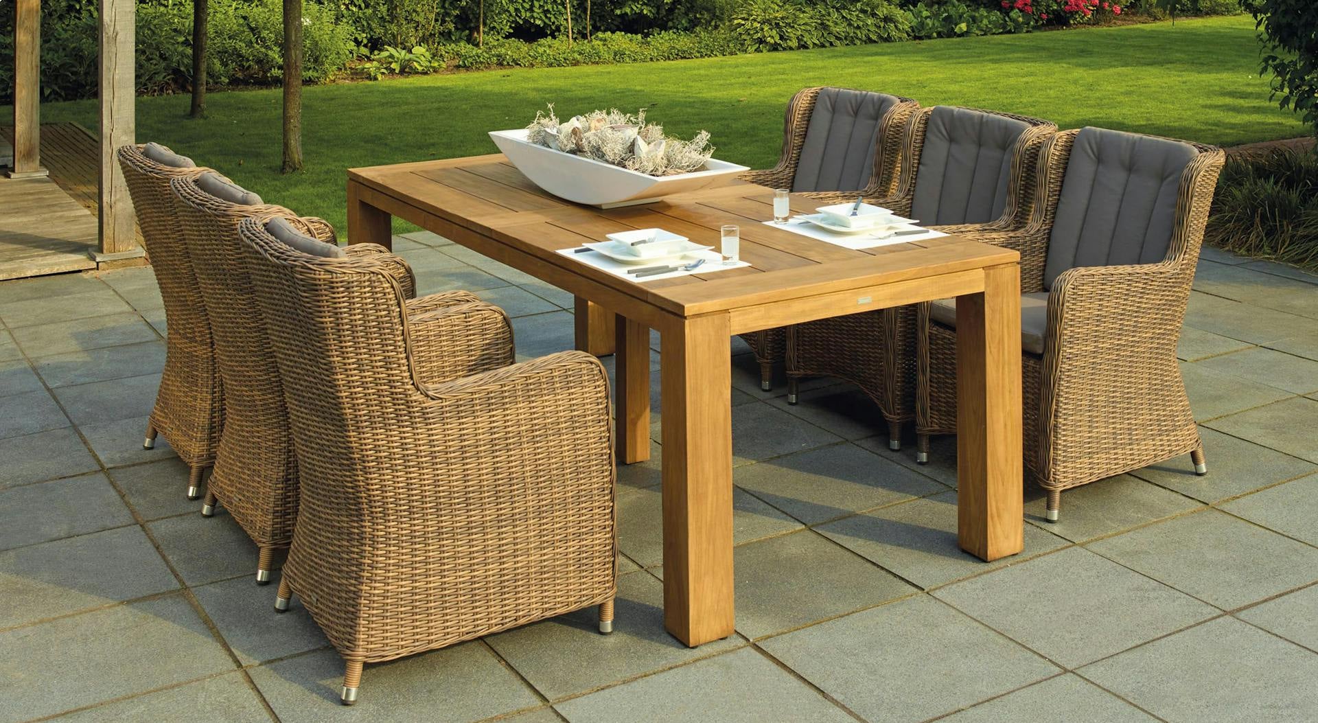 Wooden outdoor dining table with wicker chairs on a stone patio