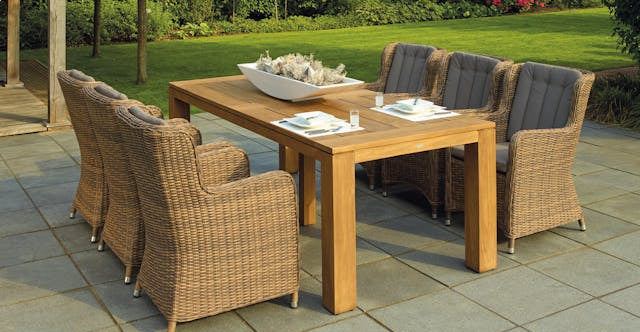 Wooden outdoor dining table with wicker chairs on a stone patio
