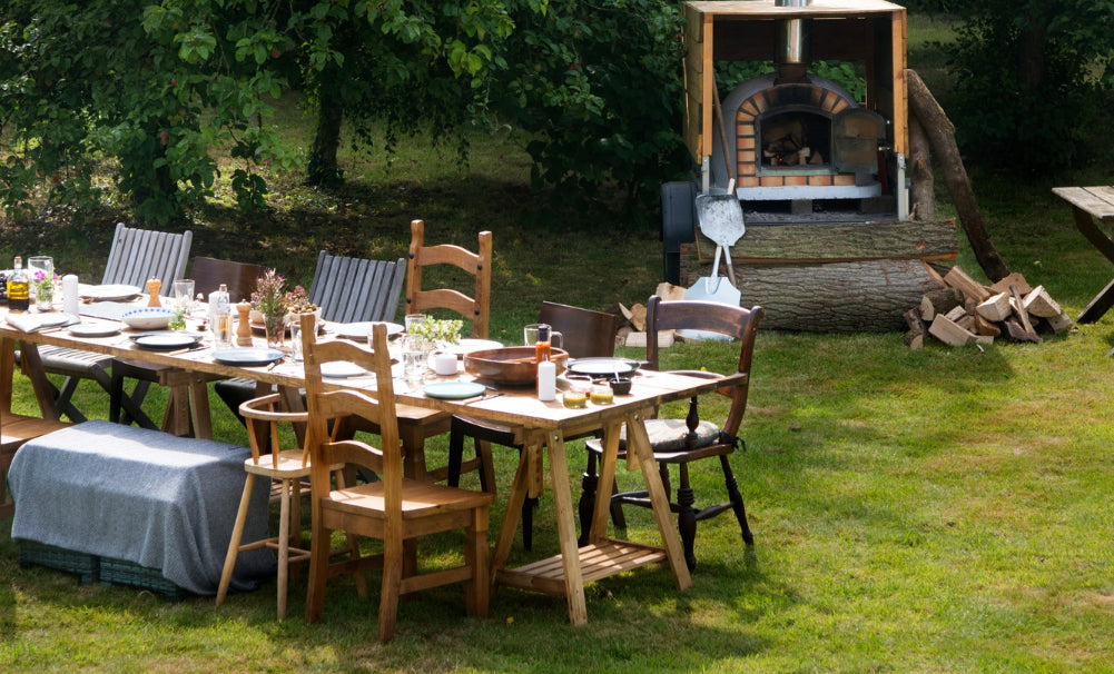 Outdoor setting with a wooden table, chairs, and a smoking barbecue grill in a garden.